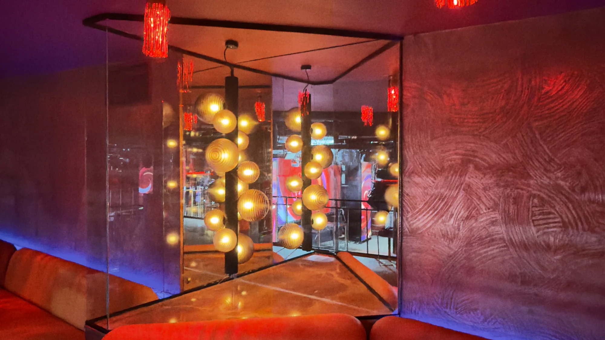 Espejos con luces esféricas doradas, sofá rojo y pared de textura en el interior de Sala Chango Madrid.