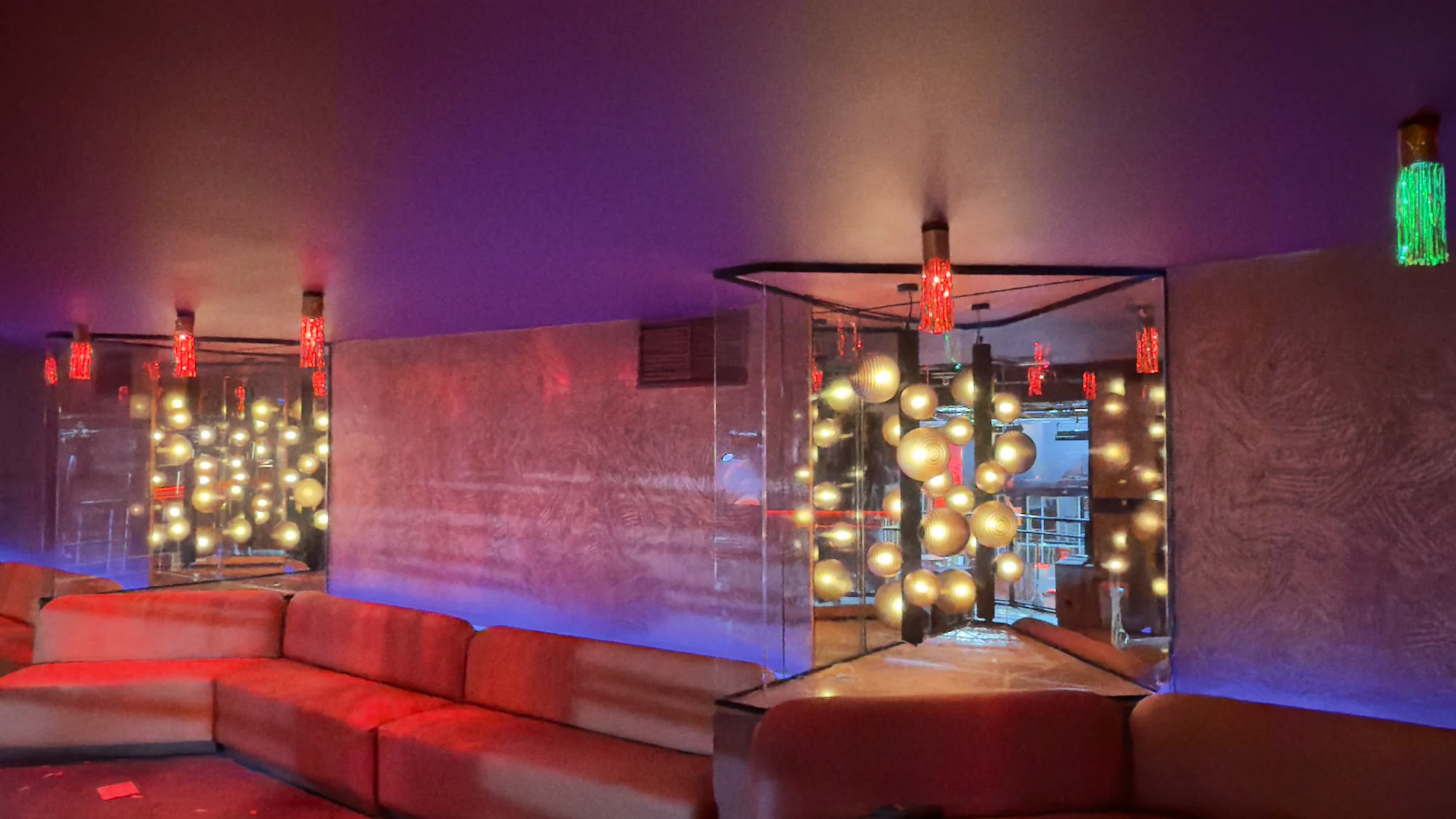 Zona de sofás con iluminación roja y morada y luces doradas en Sala Chango Madrid.