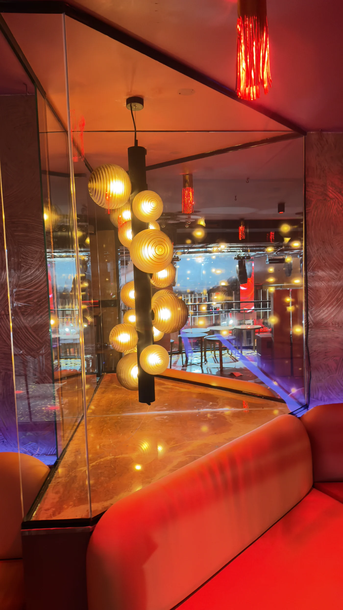 Zona elevada con sofá rojo, lámpara de esferas doradas y vista a la sala.